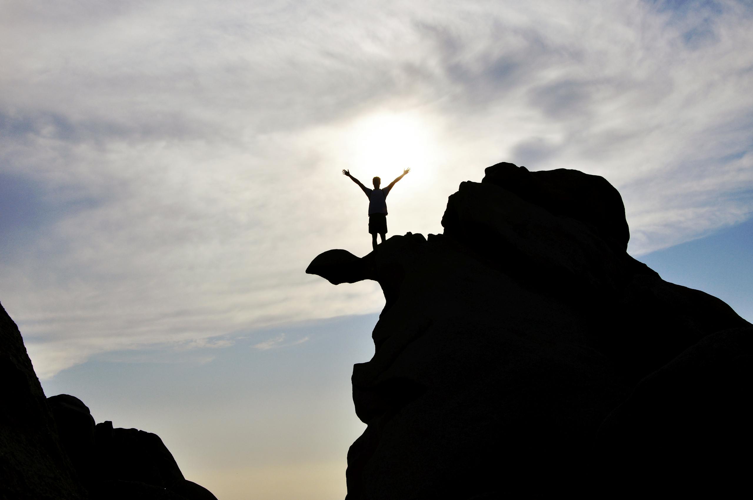 Silhouette of a person celebrating on a mountain peak against a dramatic sky, symbolizing freedom and success.
