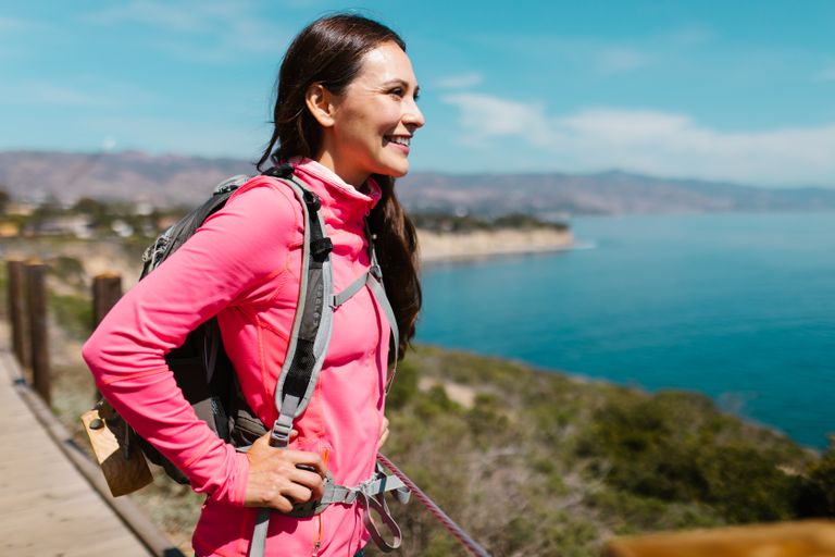 Woman in pink jacket enjoying a coastal hike with ocean view.